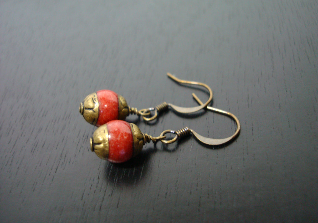 A pair of Tibetan brass capped coral earrings laid down on a dark wooden background.  Their color is a soft orange pink color made with antique gold plated ear wires.