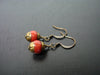 A pair of Tibetan brass capped coral earrings laid down on a dark wooden background.  Their color is a soft orange pink color made with antique gold plated ear wires.